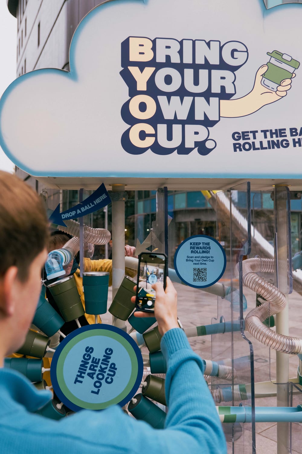 Over the shoulder shot of person holding up their phone to a QR code on Hubbub's Bring Your Own Cup installation.