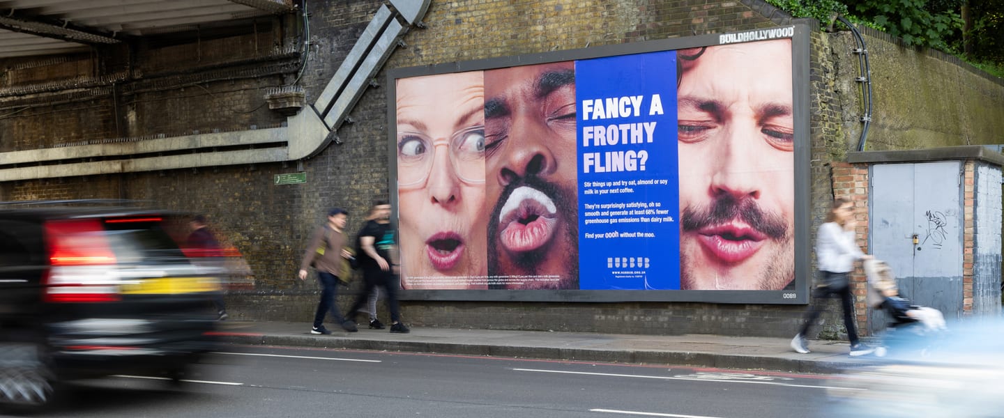 A large billboard under a bridge featuring three people with playful expressions - one of the men also has a milk moustache. Large text reads 'Fancy a frothy fling?'.