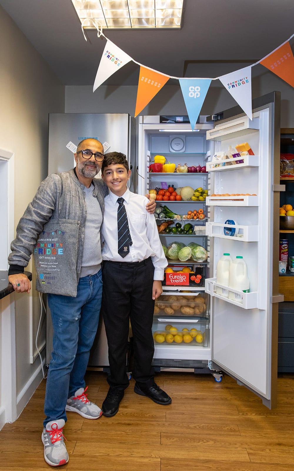 Two people stood next to an open fridge full of food at one of Hubbub's Community Fridges.