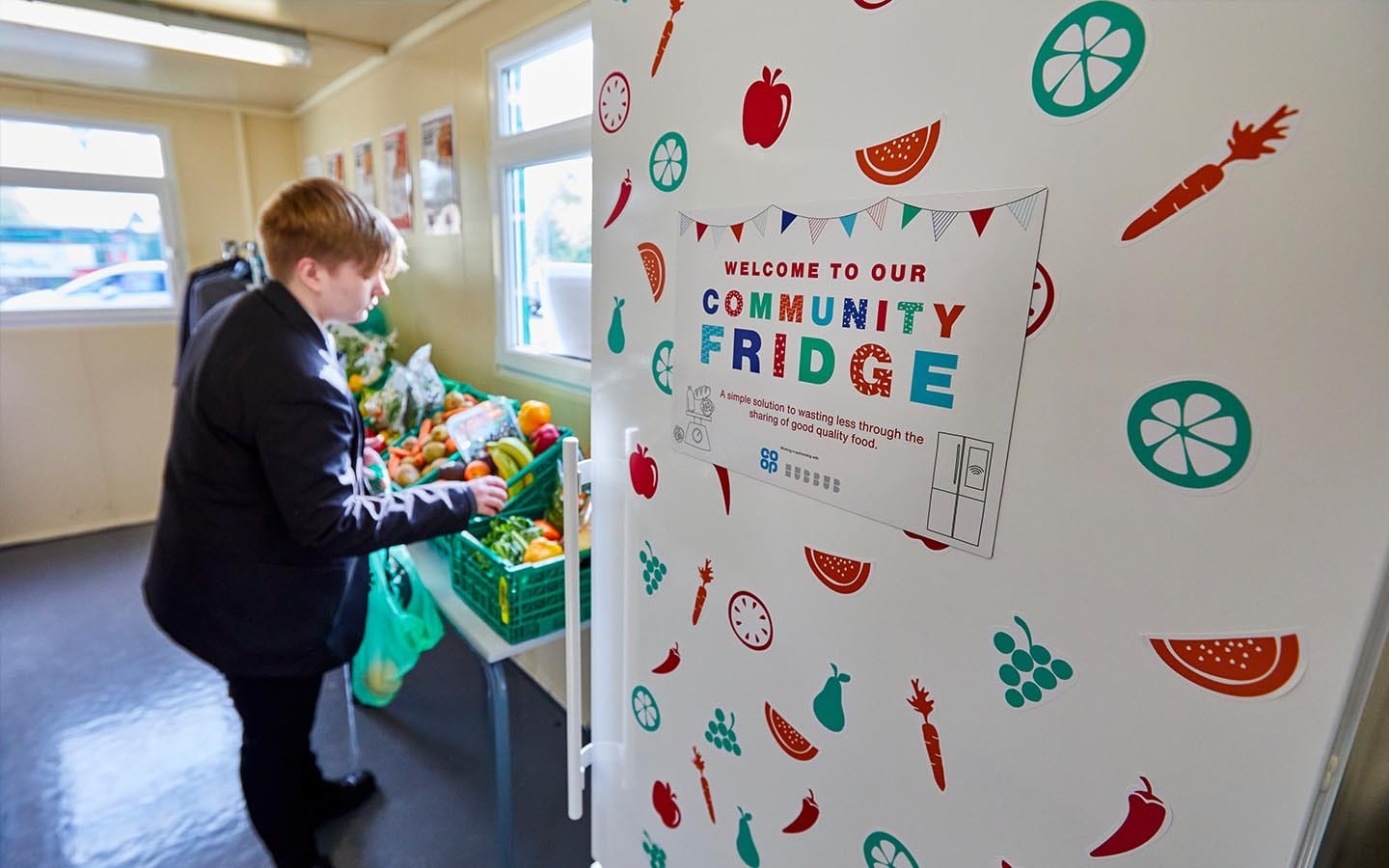 A high school student picking out some fresh fruit and vegetable items from a community fridge.