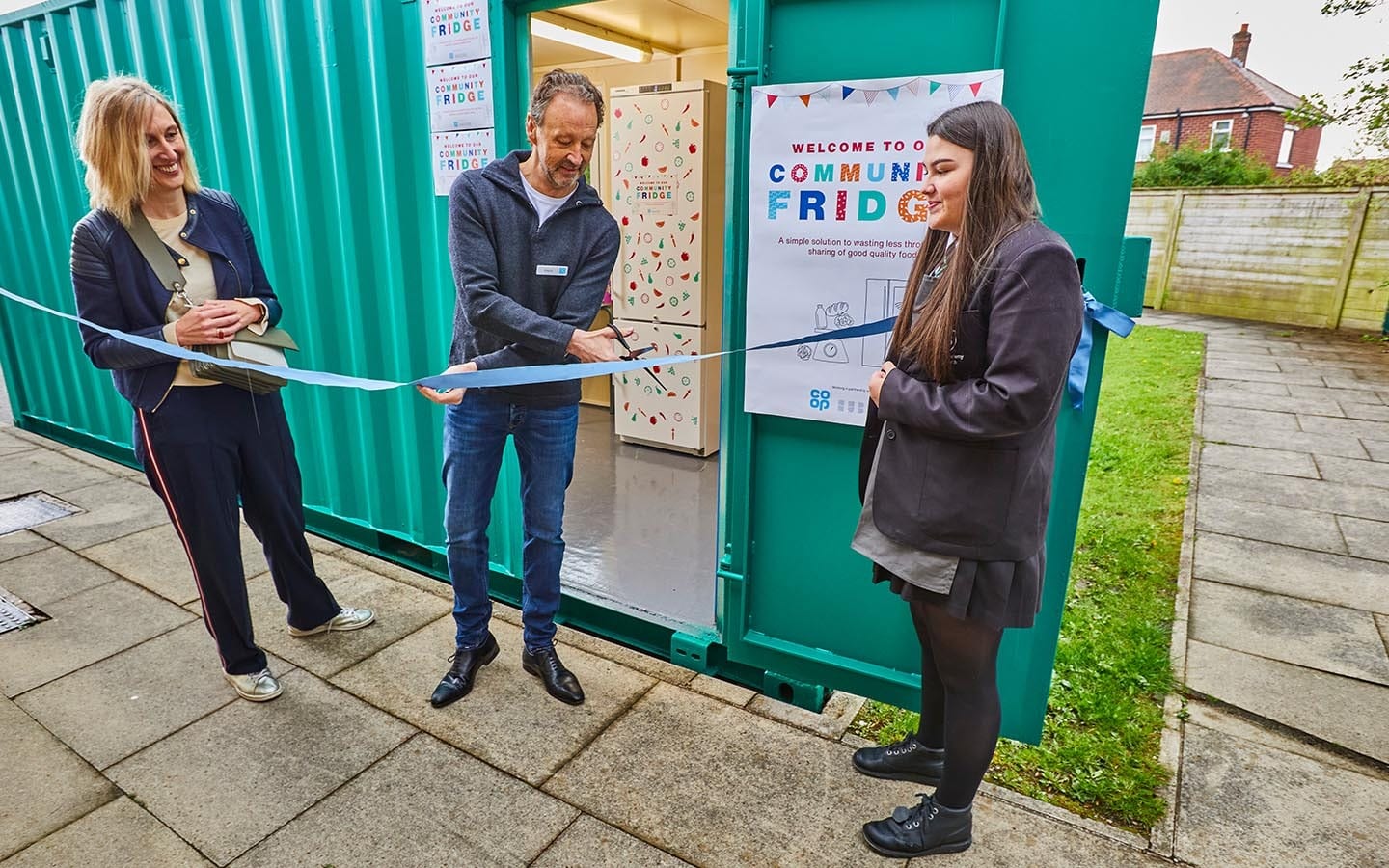 Someone cutting a ribbon at a new Community Fridge opening event.