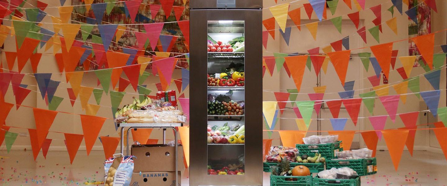 A community fridge, filled with food and decorated with lots of colourful bunting.