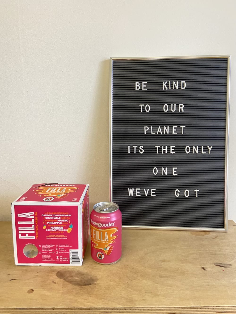 A hot pink 4-pack of beer, with bold lettering reading 'Brewgooder FILLA'. A sign also reads 'be kind to our plate, it's the only one we've got'