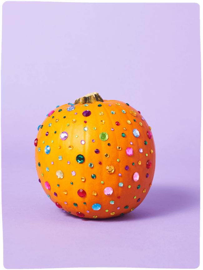 A pumpkin decorated with colourful rhinestones sat against a light purple backdrop.