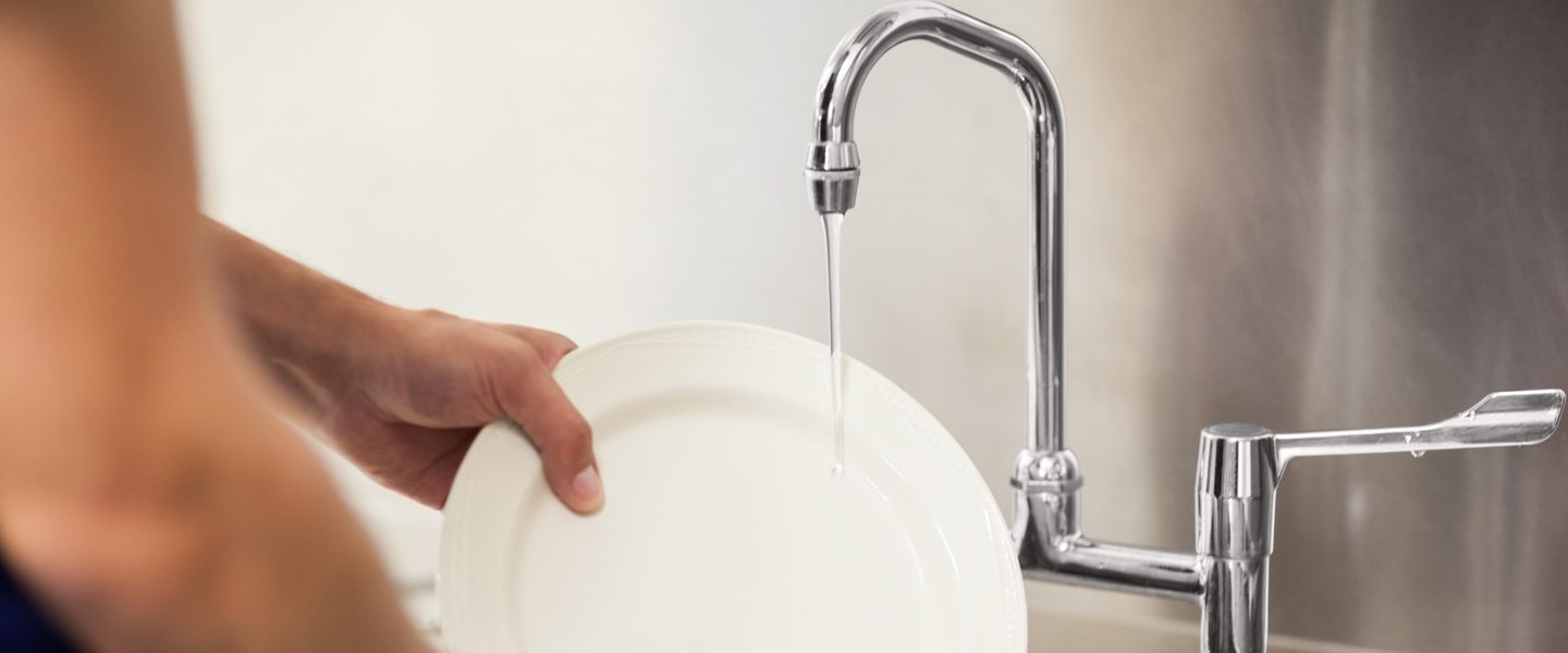 Person washing a white plate in a sink with a running tap