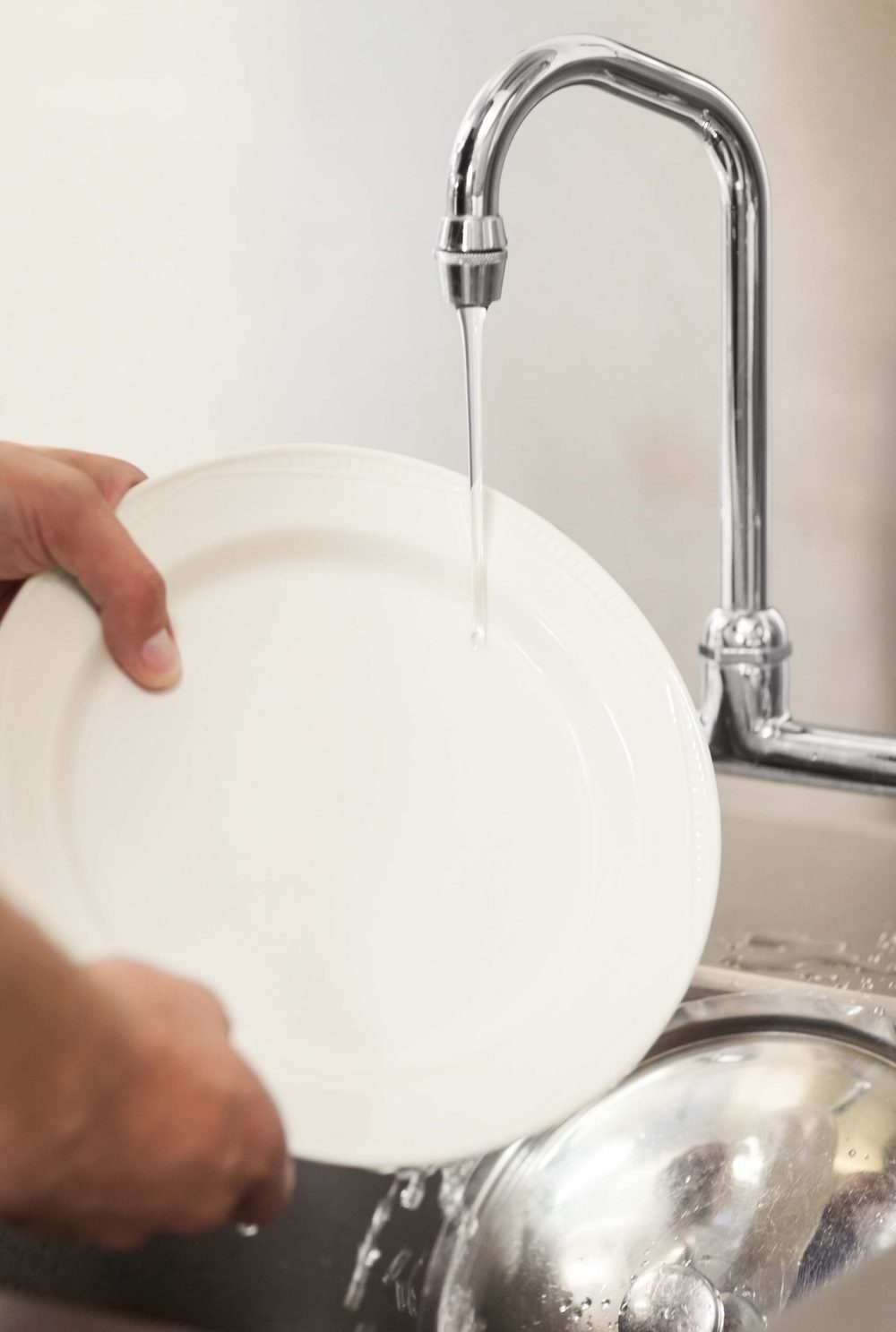Close up of person holding a white plate under a tap with the water running