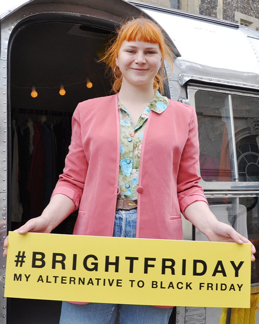 A young woman with ginger hair is smiling and holding a sign that says '#BrightFriday My alternative to Black Friday'.