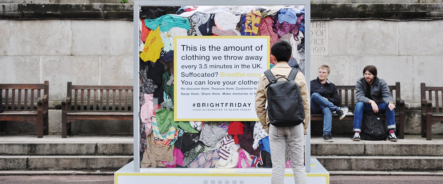 A man stood observing a large installation about Hubbub's Bright Friday campaign. The installation is a large transparent cube filled with clothes showing the amount of clothing that is thrown away every 3.5 seconds in the UK