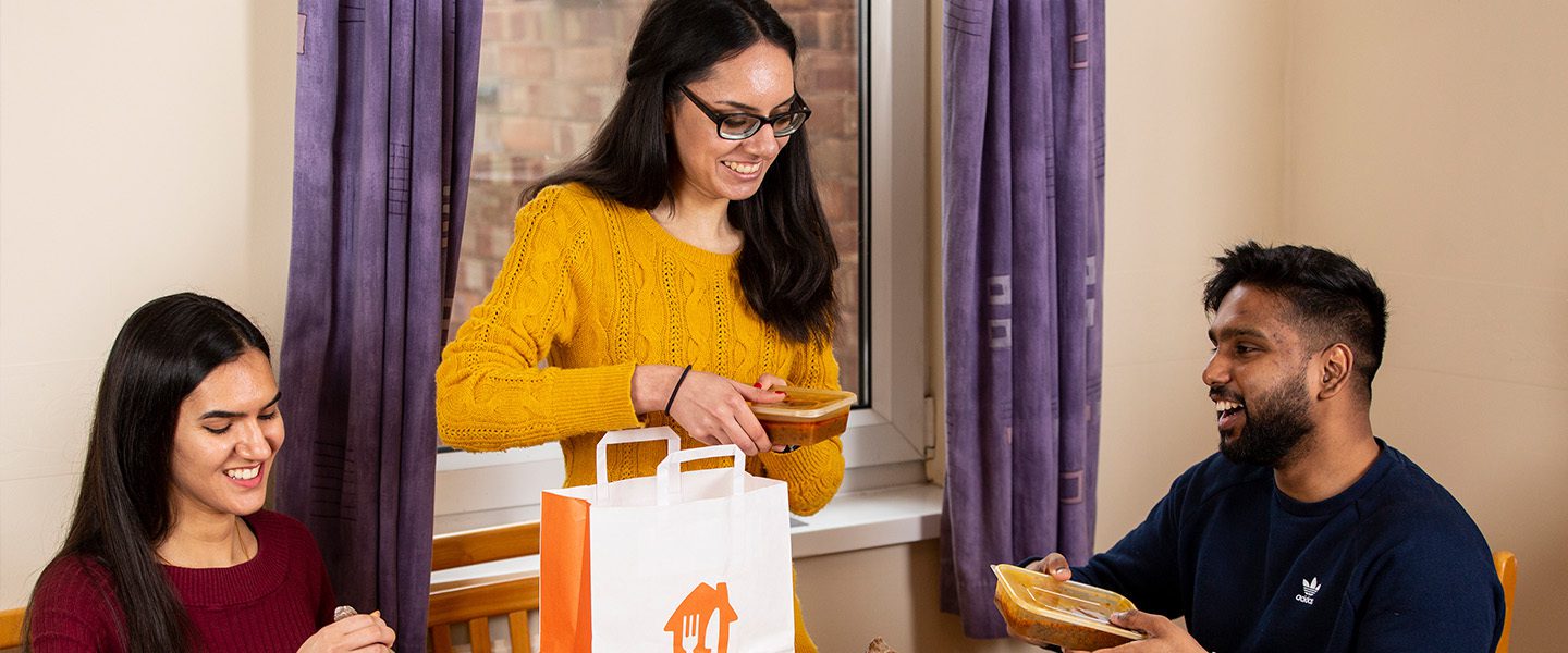 A group of friends sat around a table dishing out a Just Eat takeaway.