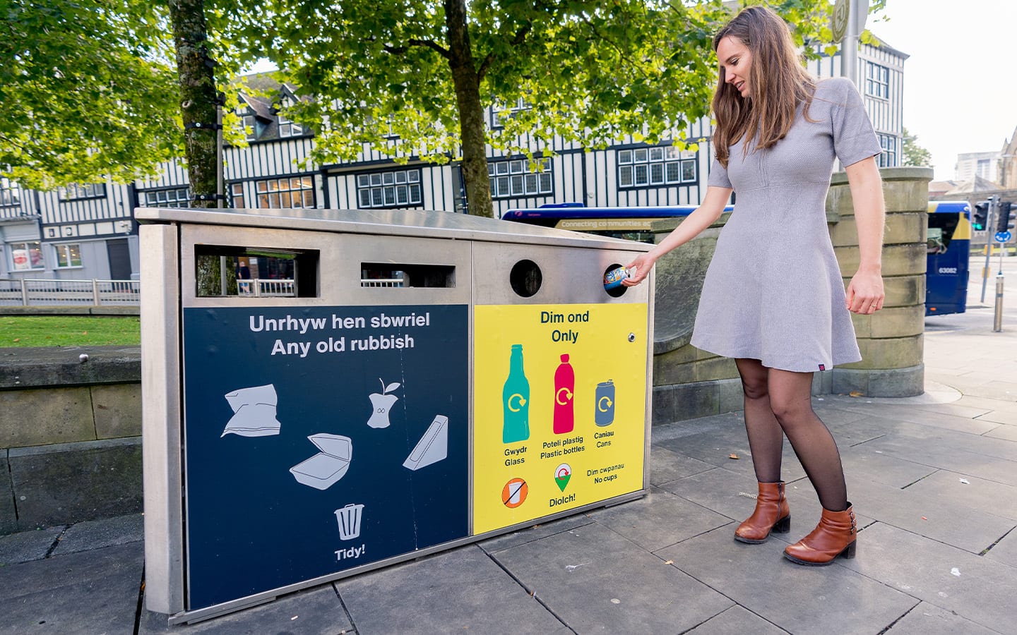 A young woman putting recycling into an on street In The Loop yellow recycling bin.