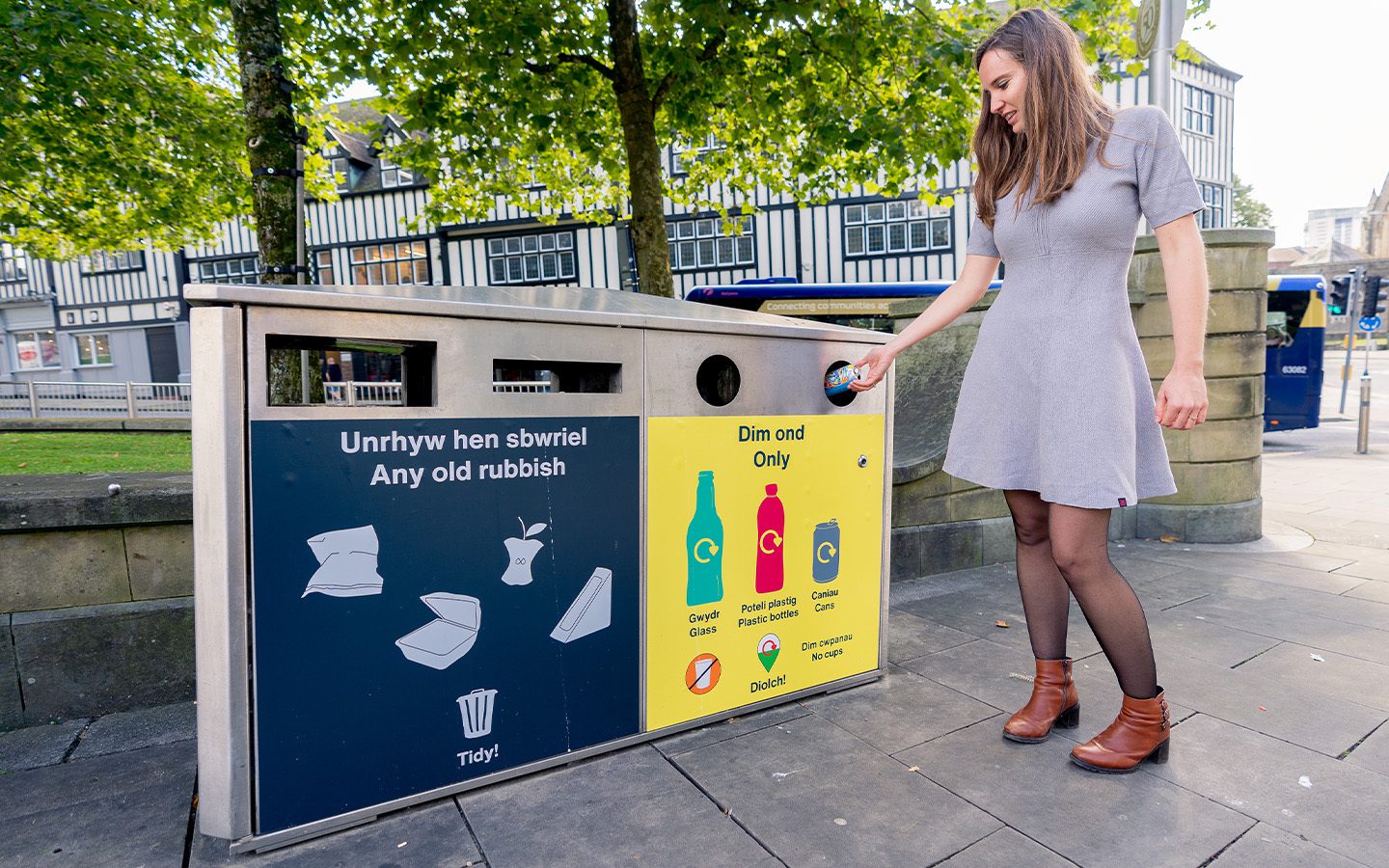 A young woman putting recycling into an on street In The Loop yellow recycling bin.