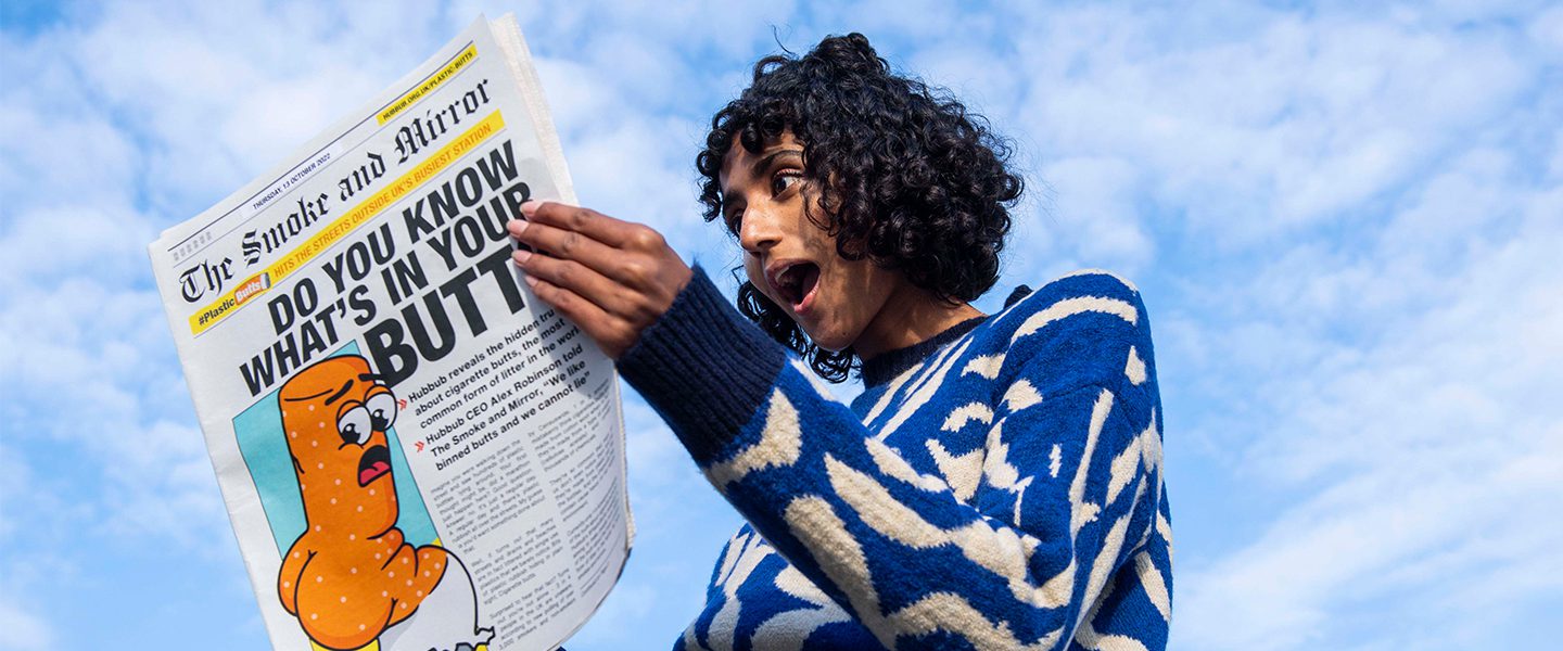 Someone looking surprised whilst holding up a newspaper which details a story about the amount of plastic found in cigarette butts.