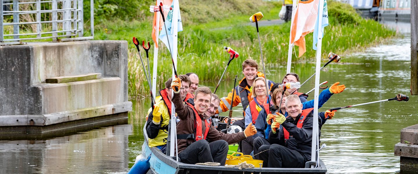 A group of people out on a Plastic Fishing boat. They have their litter pickers in the air showing what the litter they have 'fished' out of the water.