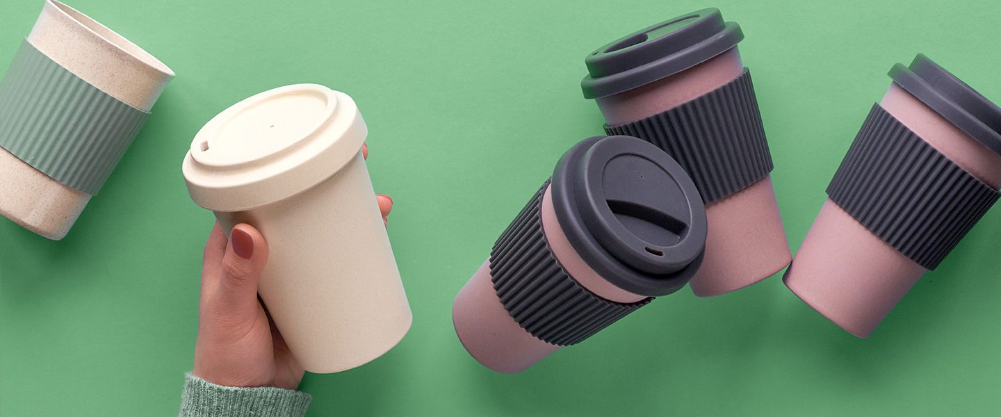 A selection of reusable coffee cups and a hand reached out to take one.