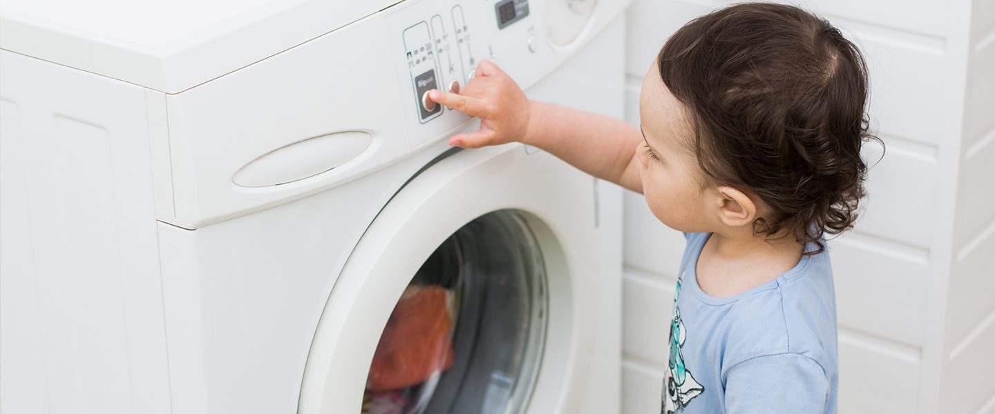 A toddler is pressing buttons on a washing machine.
