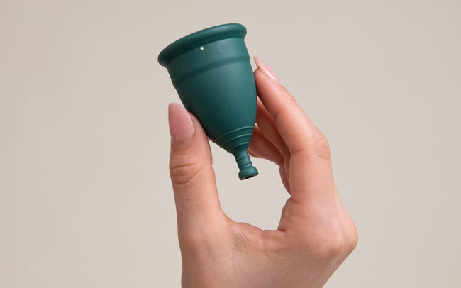 A woman's hand holding up a green menstrual cup.