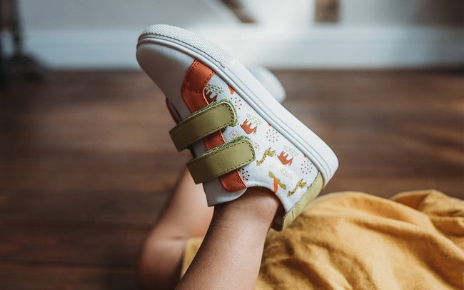 A child's is lying on the floor with their shoes in the air.