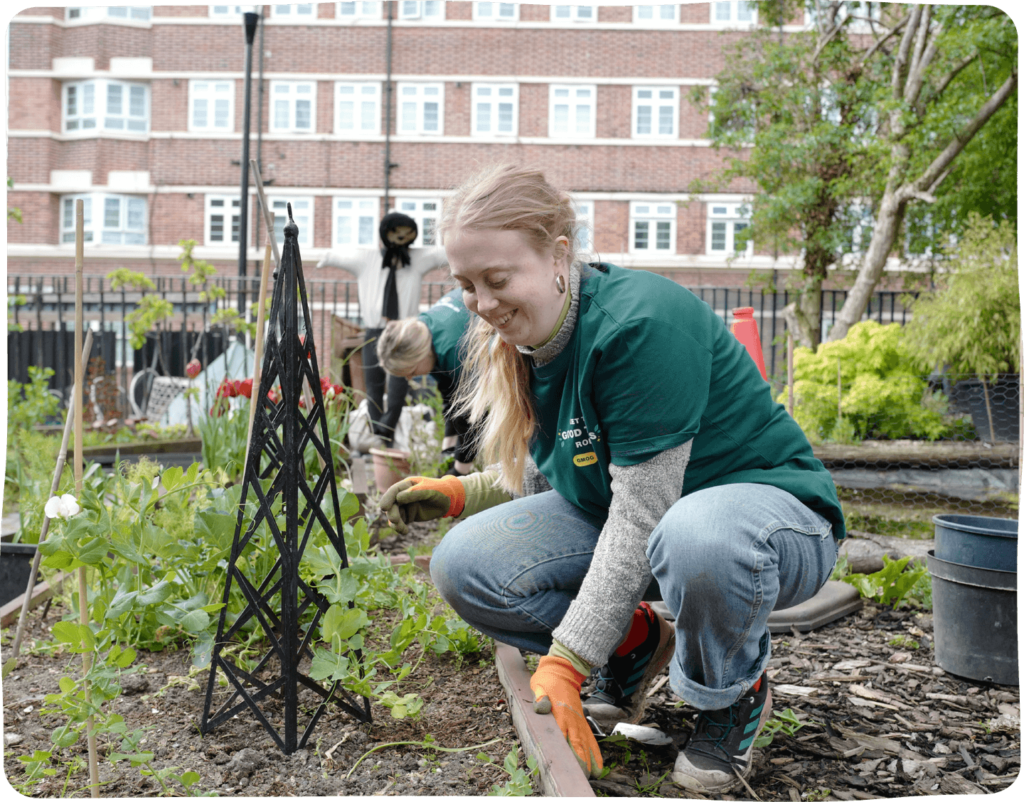 A young women crouches down in a gardening patch.