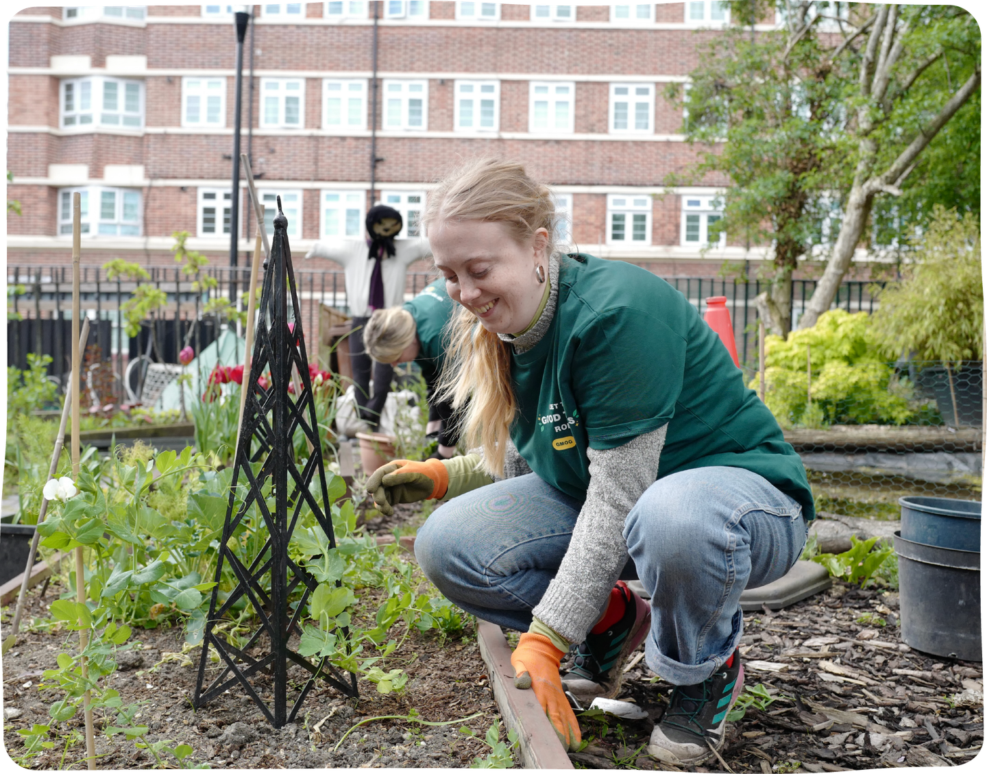A young women crouches down in a gardening patch.