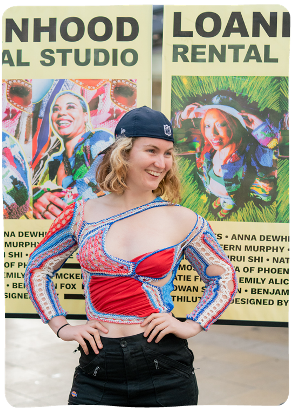 A young blonde woman smiles and poses in front of rollout banners that read 'Loanhood rental studio'. She is wearing a stylish red and blue top with cutout sections over the shoulders and arms.