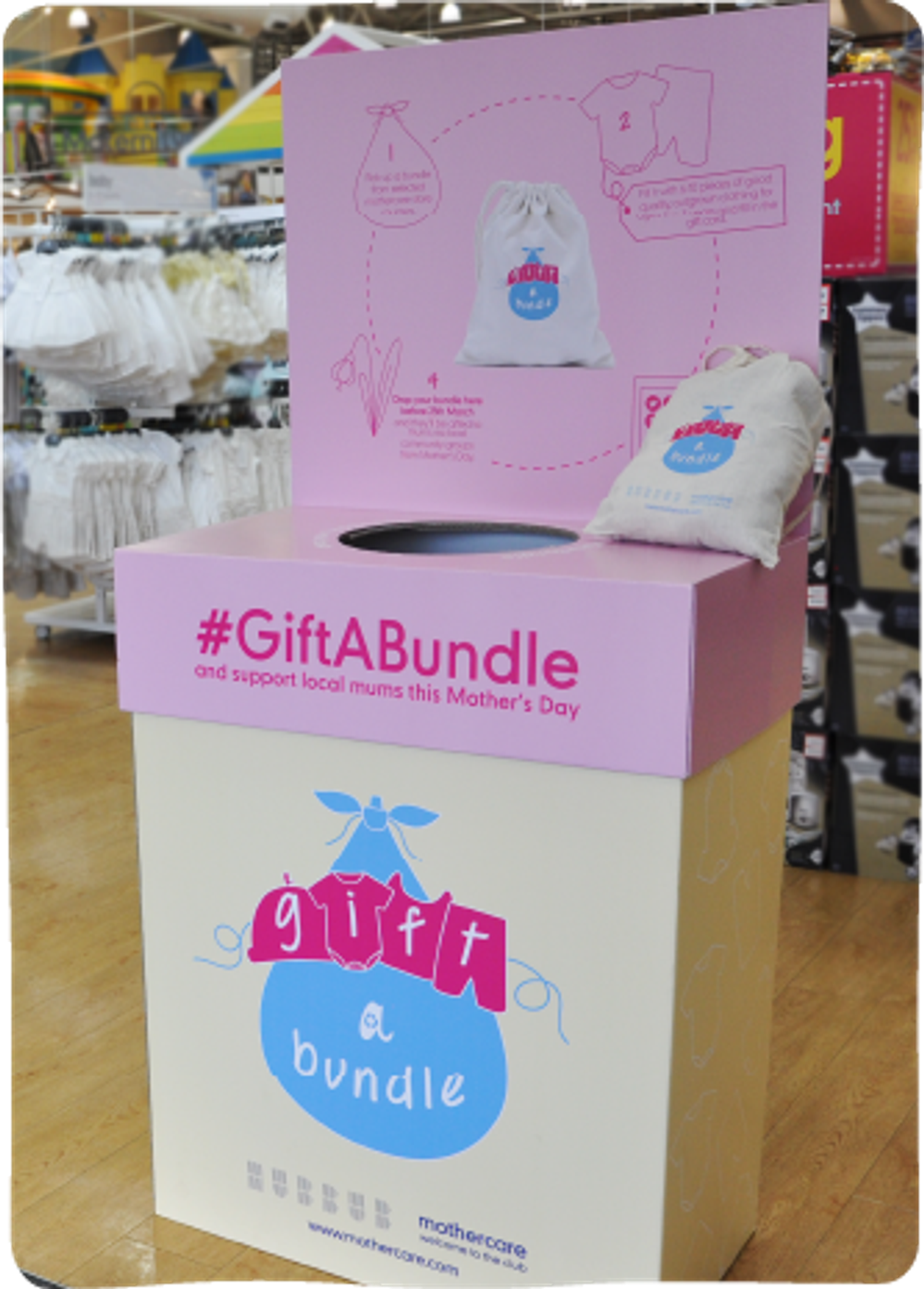 A donation station placed on a shop floor, in the midst of baby clothes. The station's design reads 'Gift a bundle and support local mums this mother's day'