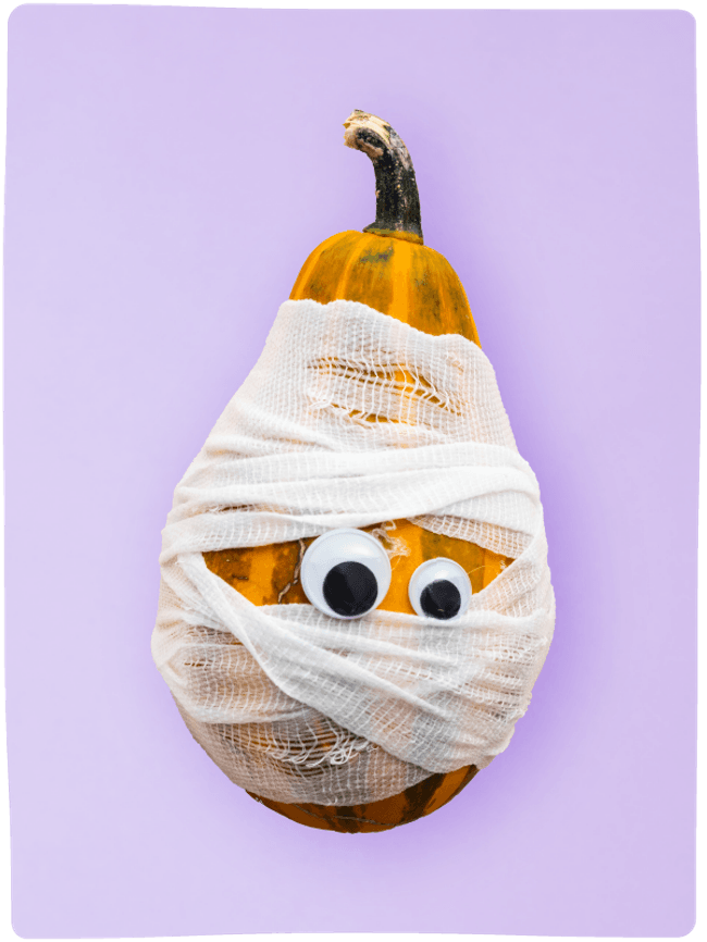 A tall orange and green pumpkin decorated as a mummy with bandages and googly eyes sat against a light purple backdrop.