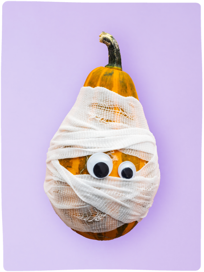 A tall orange and green pumpkin decorated as a mummy with bandages and googly eyes sat against a light purple backdrop.