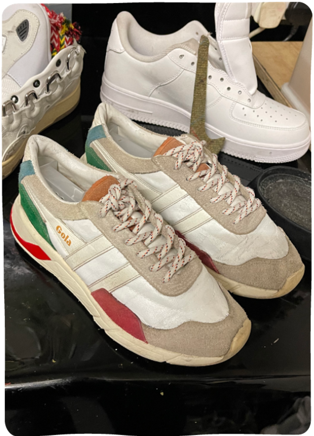 A pair of Gola trainers (white with bright colourful accents) on a workbench. The trainers are visibly not new, but look fresh and well looked after.