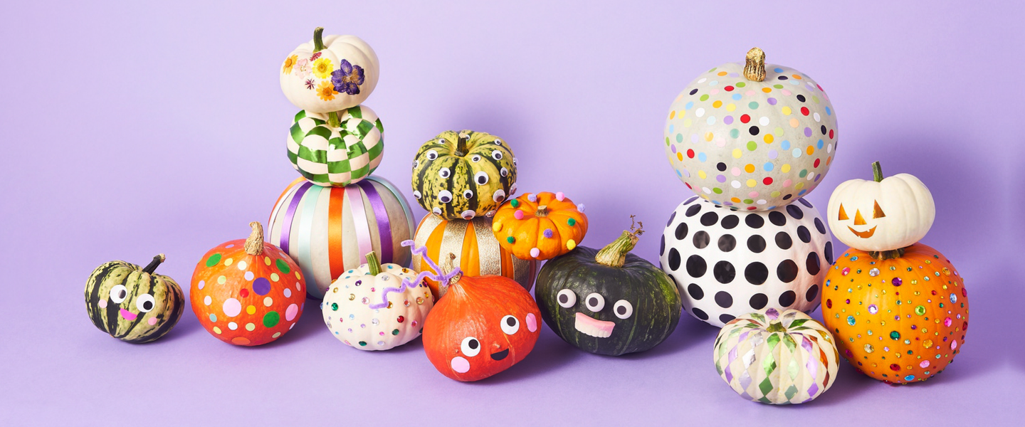 A bunch of colourfully decorated pumpkins sat against a light purple backdrop.