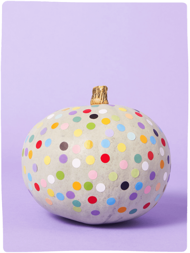 Pale green pumpkin decorated with colourful dots sat against a light purple backdrop.