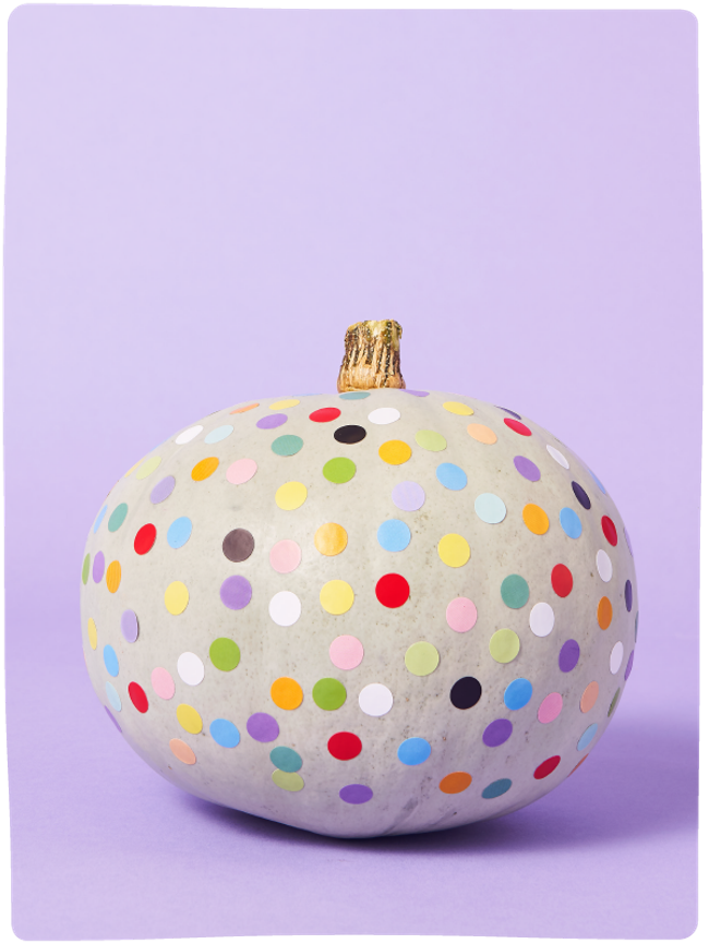 Pale green pumpkin decorated with colourful dots sat against a light purple backdrop.